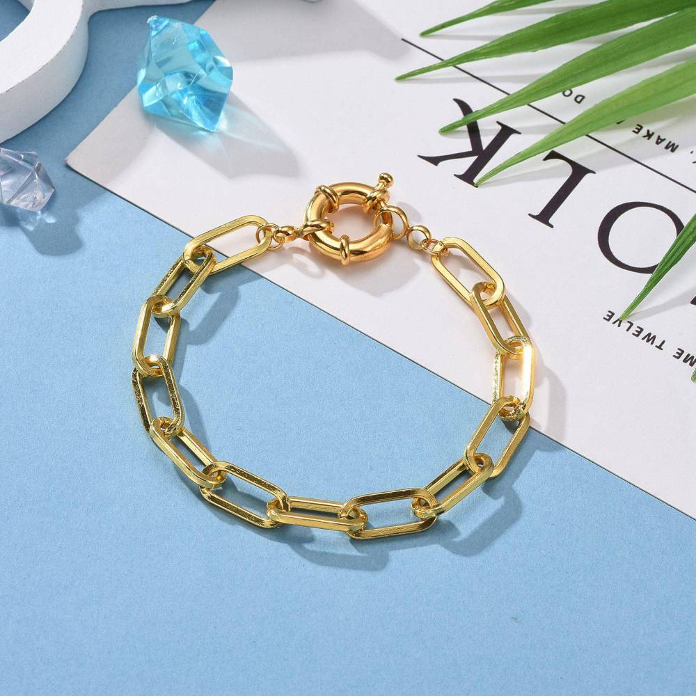 golden paperclip link bracelet with large spring ring clasp on blue and white background. 