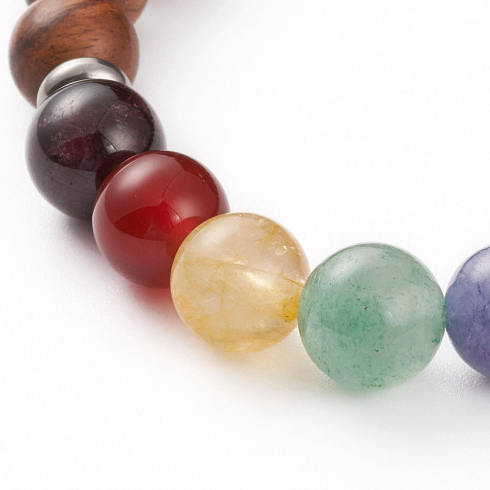 zoomed in section of wooden chakra bead stretch bracelet with seven round chakra stone beads between silver spacer bead over white background.  