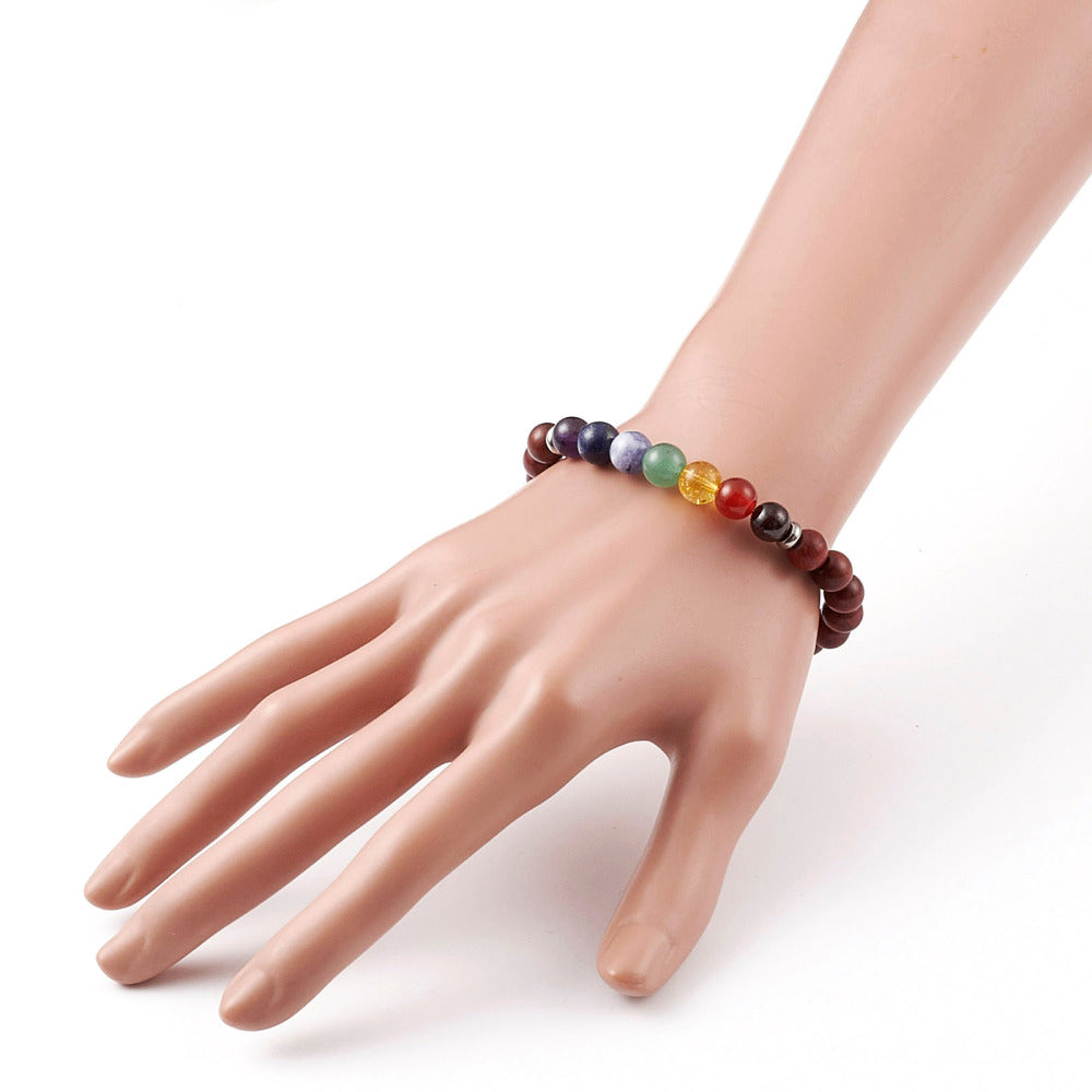 zoomed in section of wooden chakra bead stretch bracelet with seven round chakra stone beads between silver spacer bead displayed on mannequin wrist over white background.  