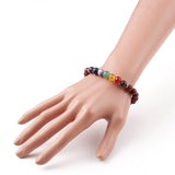 zoomed in section of wooden chakra bead stretch bracelet with seven round chakra stone beads between silver spacer bead displayed on mannequin wrist over white background.  