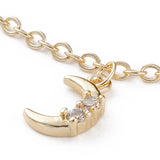 zoomed in golden moon charm with two clear round stones dangling from fine cable link chain over white background. 
