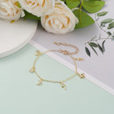 golden and clear stone charm bracelet with spring ring clasp and extender chain including a lightening bolt, star, cross, moon, padlock and crescent charms over grey, white and mint green surface with white flowers and green leaves peeking into the frame. 
