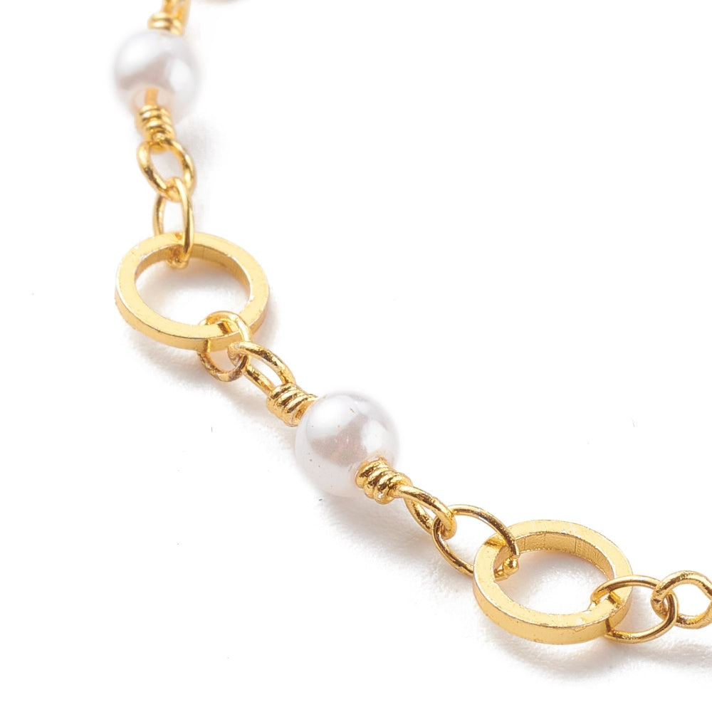 zoomed in section of golden chain bracelet alternating ring and white faux pearl links over white background.