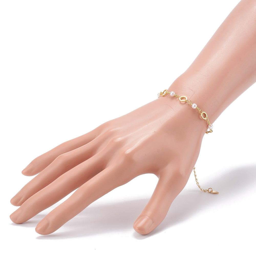 golden chain bracelet alternating ring and white faux pearl links and extender chain displayed on mannequin wrist over white background.