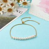 adjustable golden box chain and pearl bracelet with slider bead and bezel set clear stone stopper beads over light blue surface and white cards and flowers peeking in from the sides. 