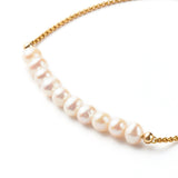 zoomed in section of golden box chain and pearl bracelet over white background. 