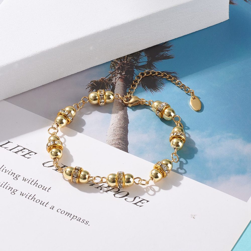 golden hematite and rhinestone link bracelet with lobster claw clasp and extender chain over a letter and picture of a palm tree with blue sky background. 