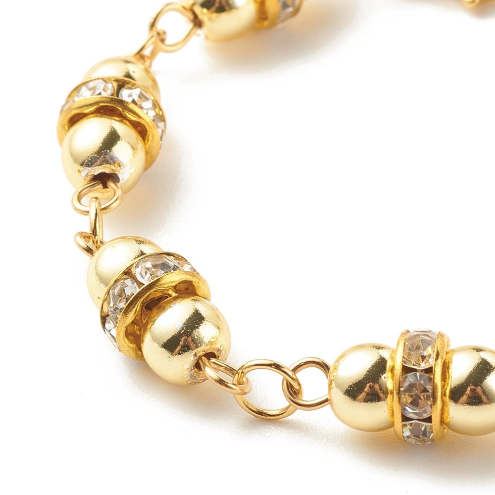 zoomed in section of golden hematite and rhinestone link bracelet over white surface. 