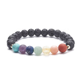 black lava rock stretch chakra bracelet featuring seven round chakra stone beads between small smooth gold spacer beads over a white background. 