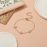 golden cable link bracelet with three white pearl beaded cross connectors a lobster claw clasp and extender chain over peach surface with colorful and white coasters peeking in the frame. 