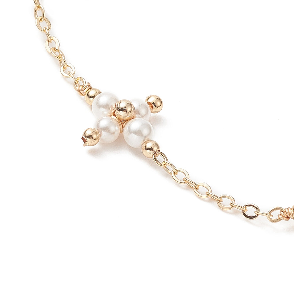 zoomed in section of golden cable link chain and white pearl beaded cross connector over white background. 