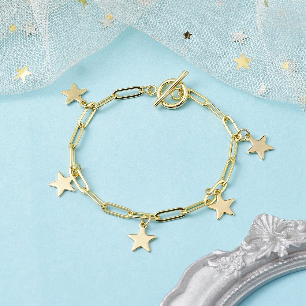 golden paperclip chain bracelet with five evenly spaced star charms and toggle clasp over light blue surface  with white tulle and an antique silver frame peeking in from the edges.