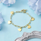 golden paperclip chain bracelet with toggle clasp and five evenly spaced heart charm dangles on a light blue surface with light blue flower petals and a silver ornate frame peeking into the frame. 