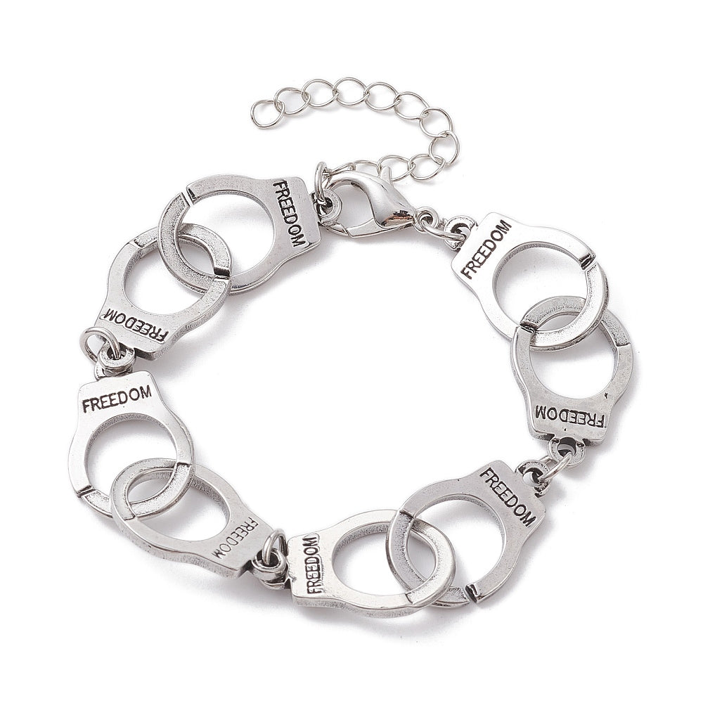 silver tone handcuff link bracelet with the word "freedom" engraved on each cuff and a lobster claw clasp and extender chain over white surface. 