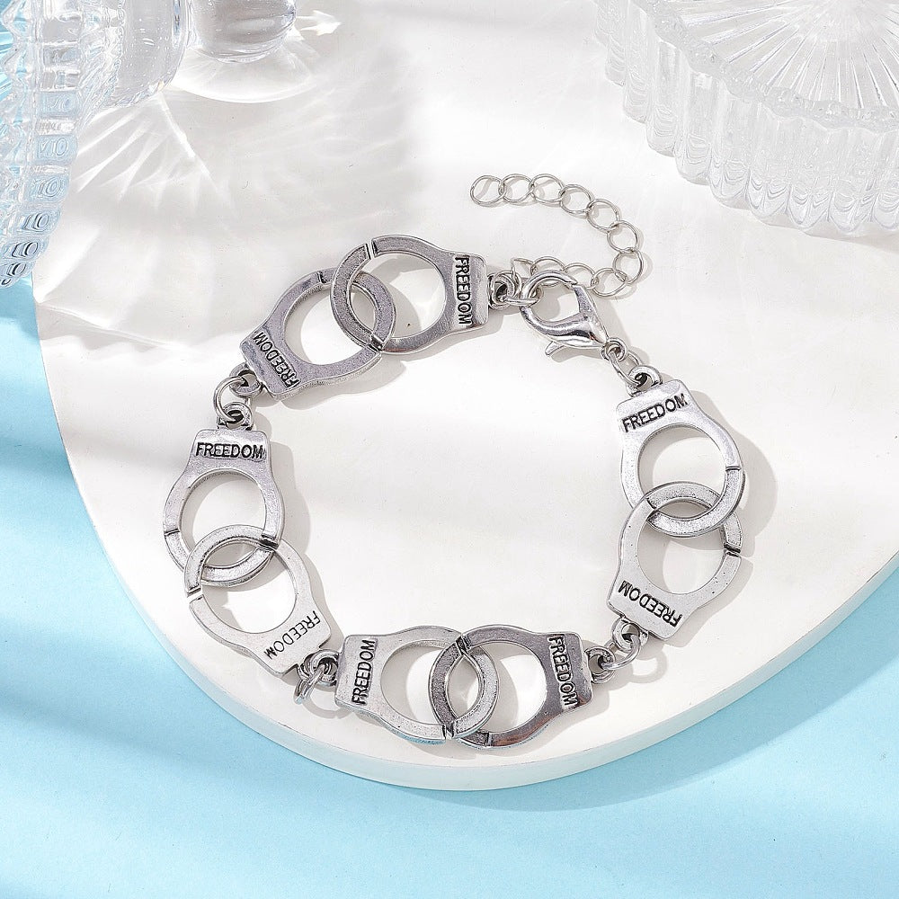 silver tone handcuff link bracelet with the word "freedom" engraved on each cuff and a lobster claw clasp and extender chain on white tray on a light blue surface.  
