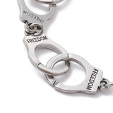 zoomed in section of silver tone handcuff link bracelet with the word "freedom" engraved on each cuff over white surface. 