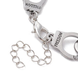 zoomed in section of silver tone handcuff link bracelet with the word "freedom" engraved on each cuff and a lobster claw clasp and extender chain over white surface. 