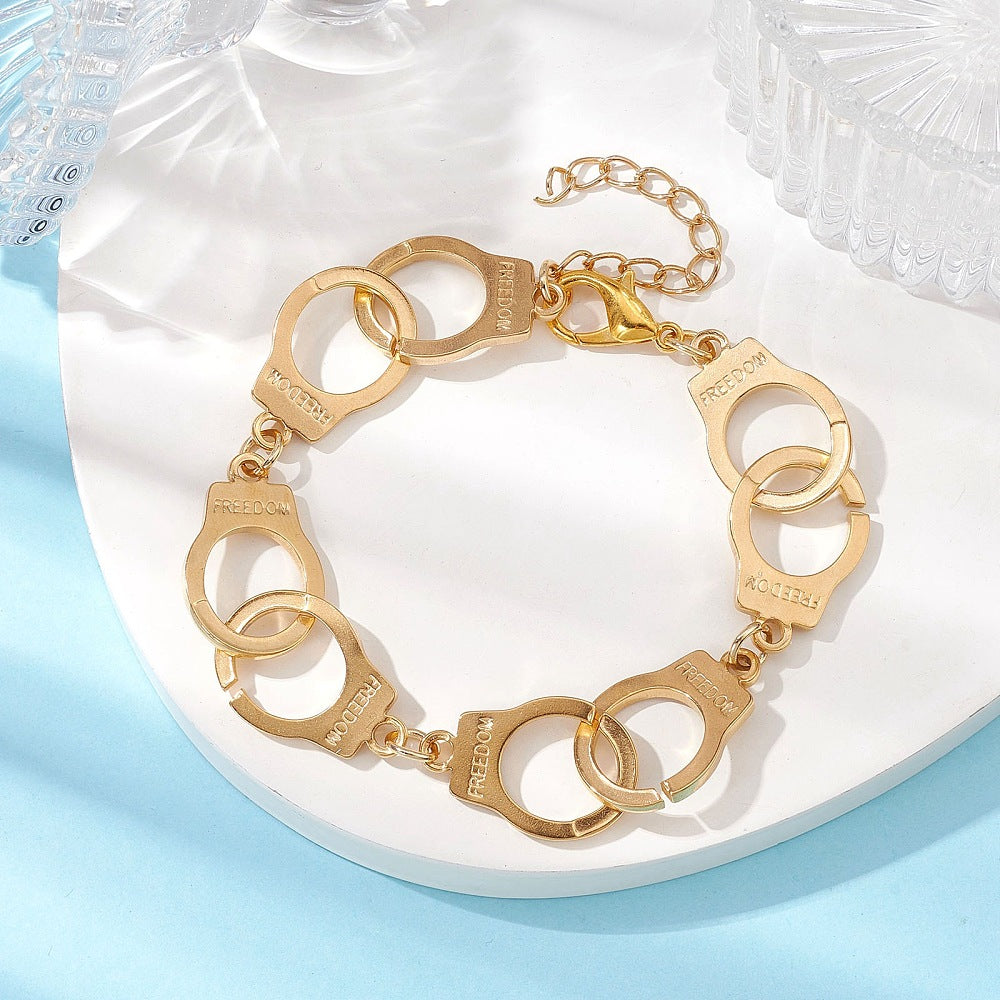 golden handcuff link bracelet with the word "freedom" engraved on each cuff and a lobster claw clasp and extender chain on white tray on a light blue surface.  