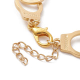 zoomed in section of golden handcuff link bracelet with the word "freedom" engraved on each cuff and a lobster claw clasp and extender chain over white surface. 