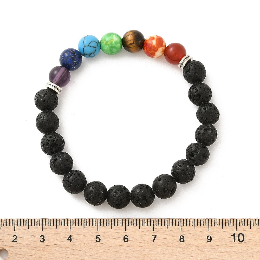 black lava rock chakra stretch bracelet featuring seven round chakra stone beads between silver double line spacer beads displayed above a wooden ruler with a white background. 