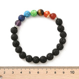 black lava rock chakra stretch bracelet featuring seven round chakra stone beads between silver double line spacer beads displayed above a wooden ruler with a white background. 