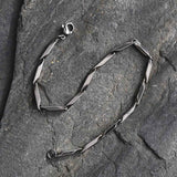 silver tone bar link chain bracelet with lobster claw clasp in "s" design on a grey rock slab. 