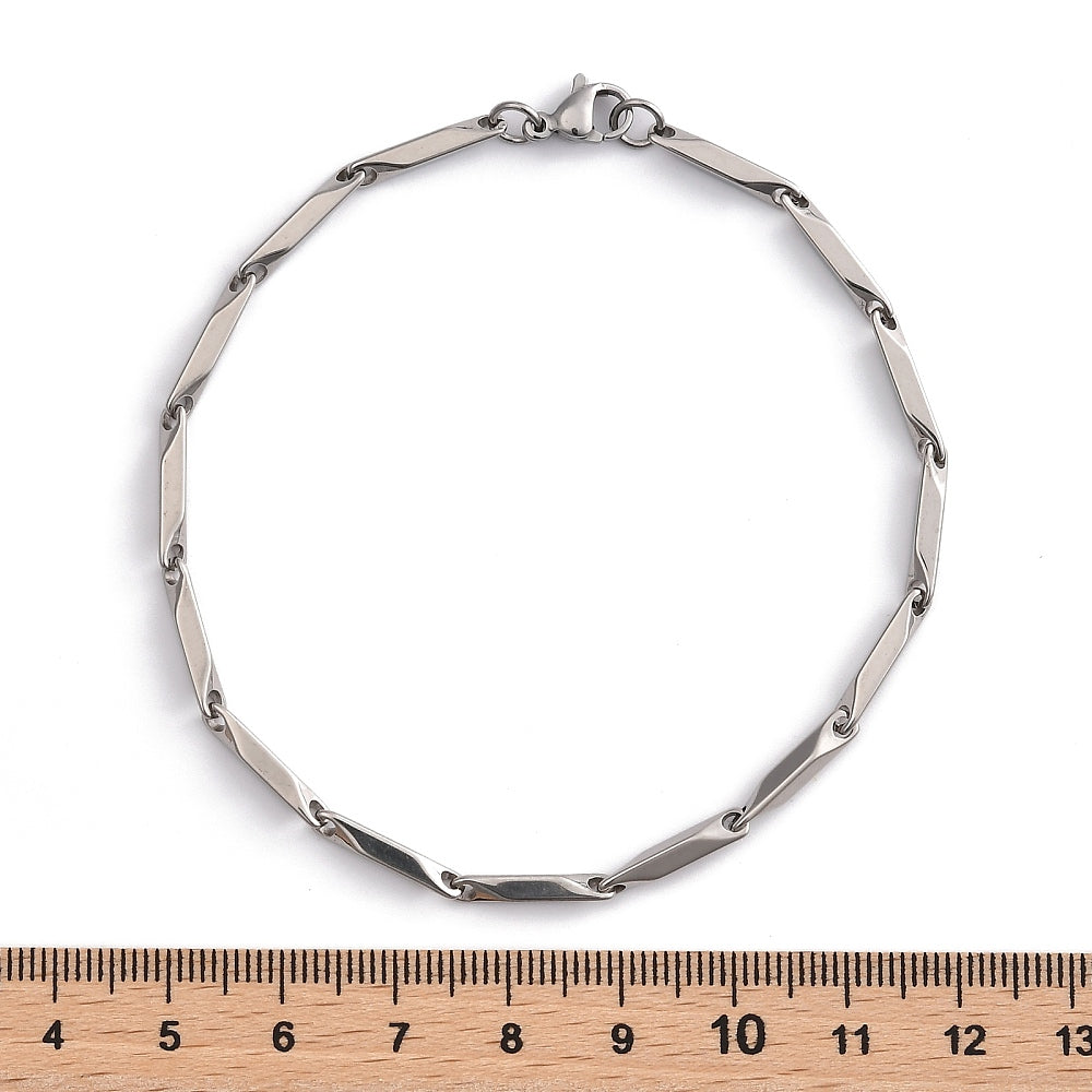 silver tone bar link chain bracelet with lobster claw clasp displayed over wooden ruler with white background. 