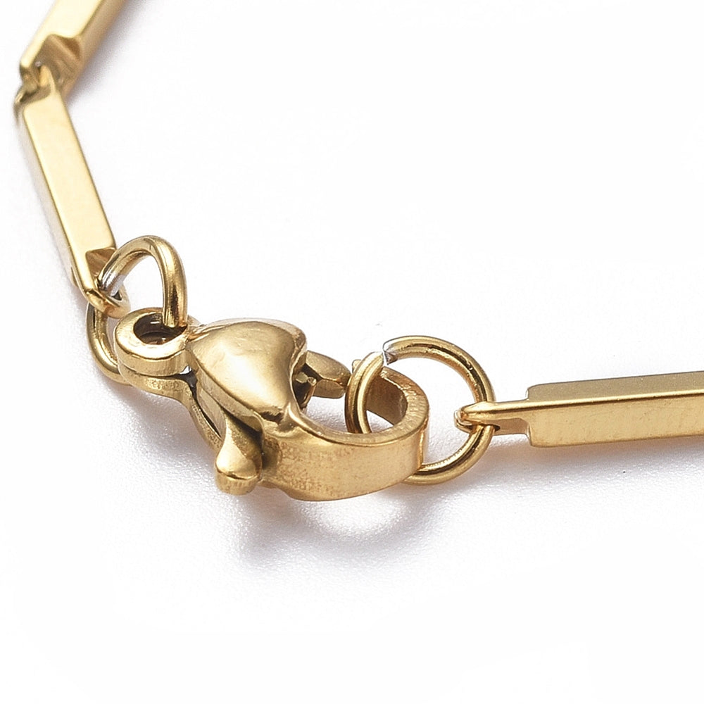 zoomed in section of golden bar link bracelet with lobster claw clasp over white background. 
