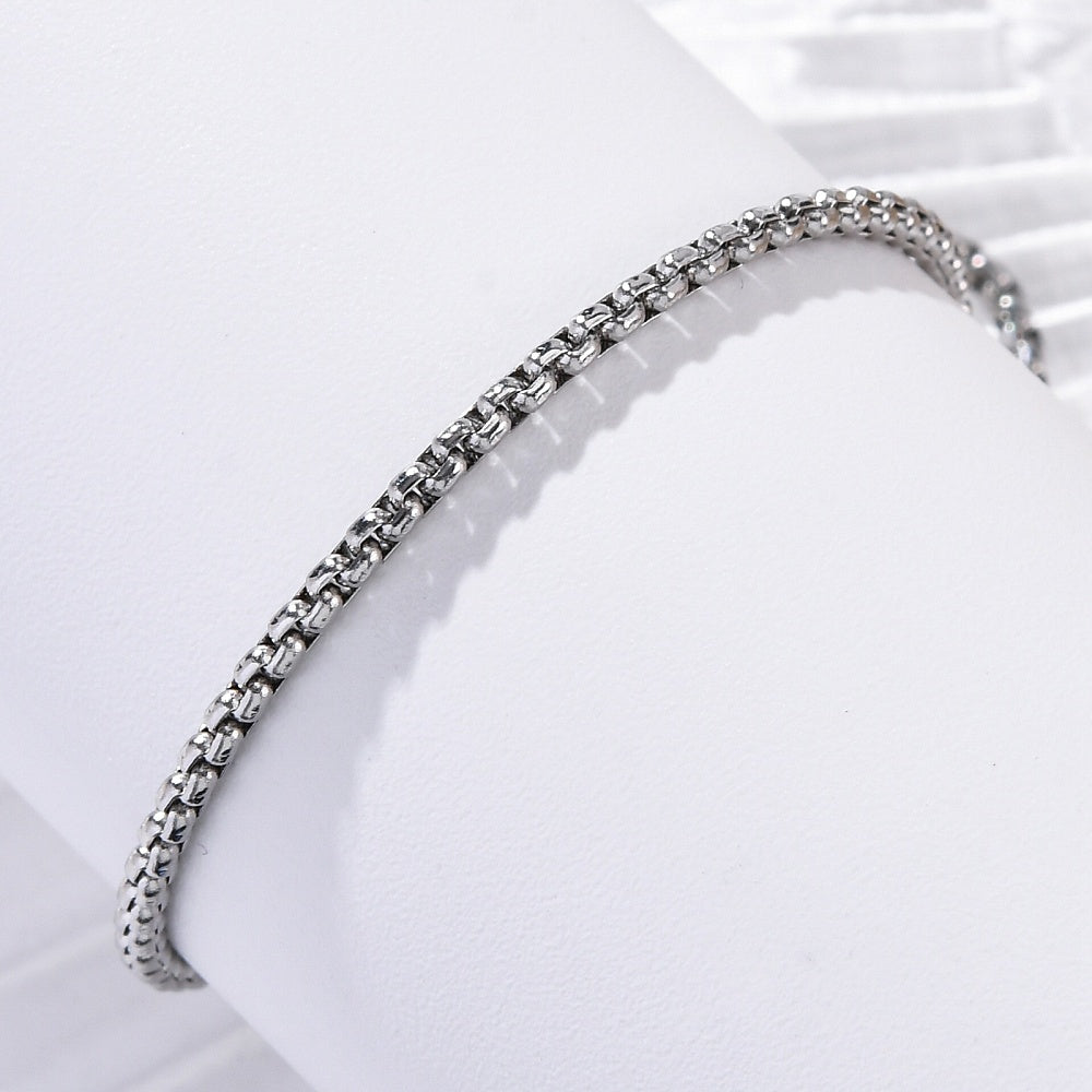 silver tone box chain draped over white cylinder with white background. 