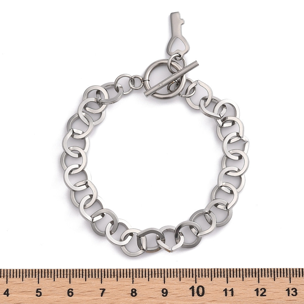 silver tone large cable link bracelet with toggle clasp and key charm displayed above a wooden ruler on white background. 