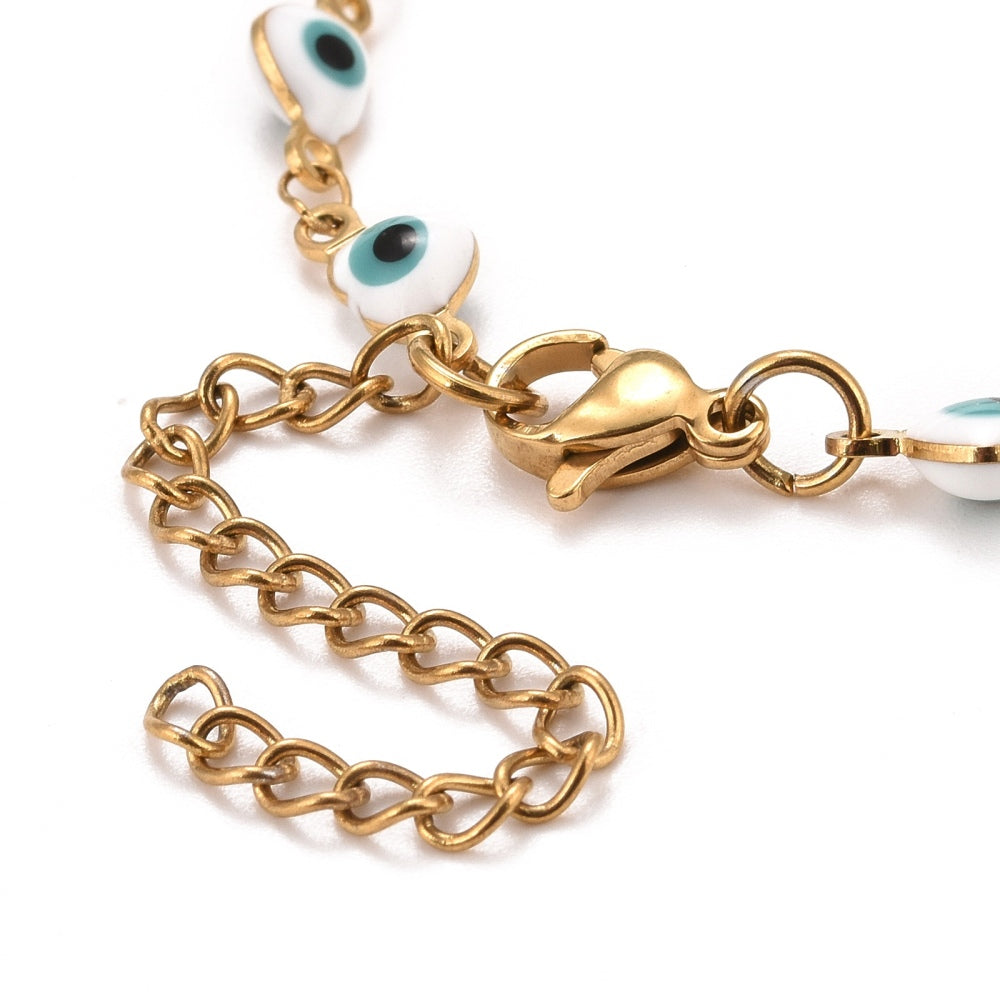 zoomed in section of golden and white enamel heart shaped evil eye bracelet with lobster claw clasp and extender chain over white background.