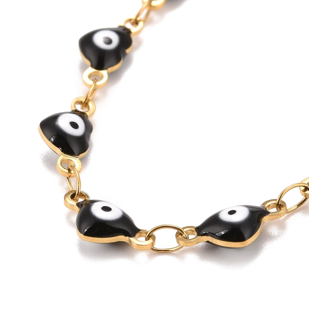 zoomed in section of golden and white enamel heart shaped evil eye bracelet  over white background.