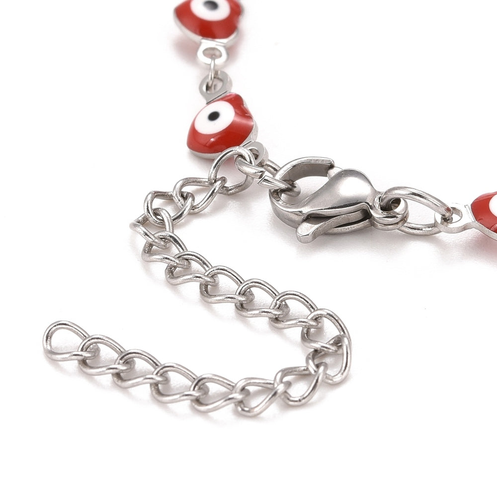 zoomed in section of silver tone and red enamel heart shaped evil eye bracelet with lobster claw clasp and extender chain over white background.