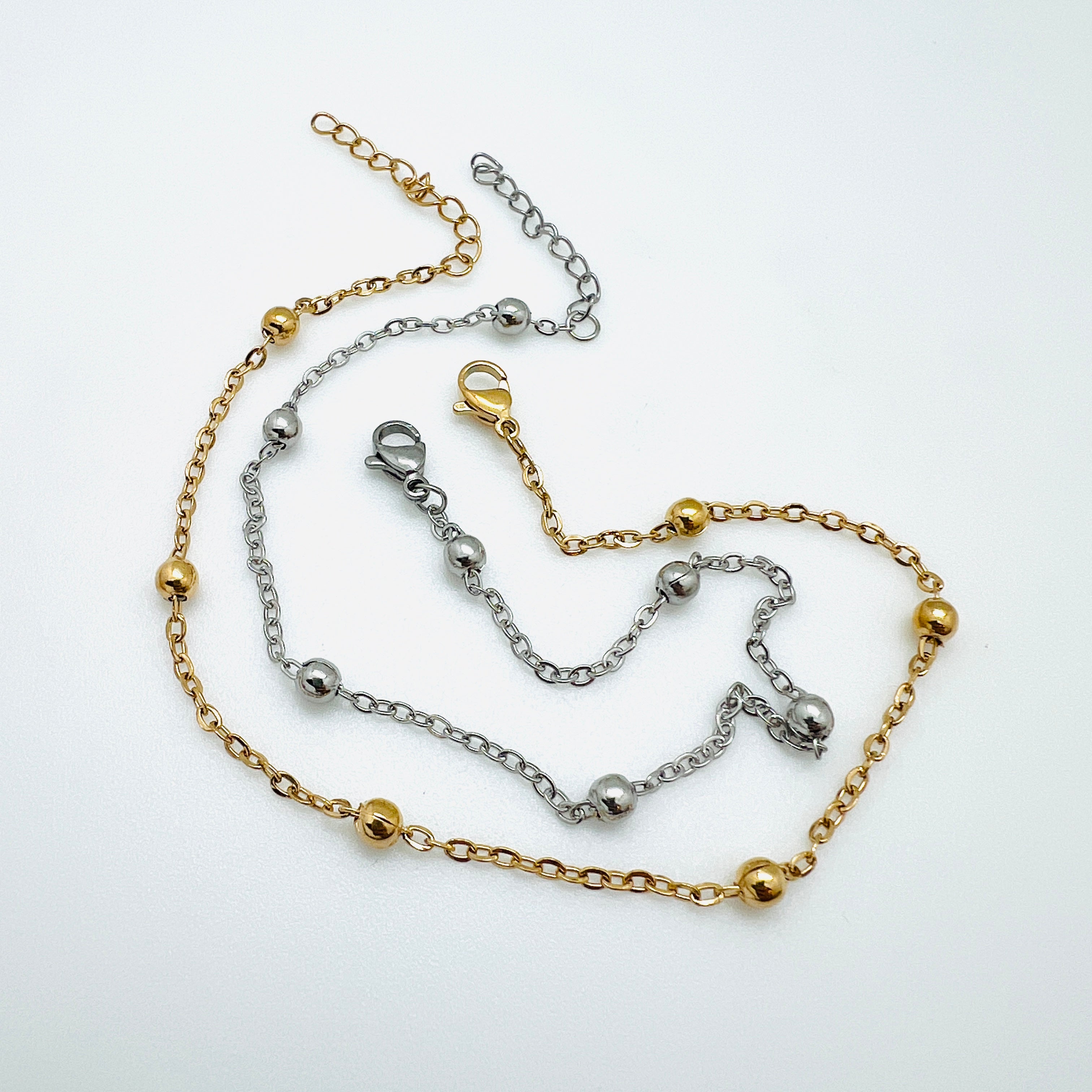 golden and silver tone satellite chain anklets with lobster claw clasp and extender chain over white background. 