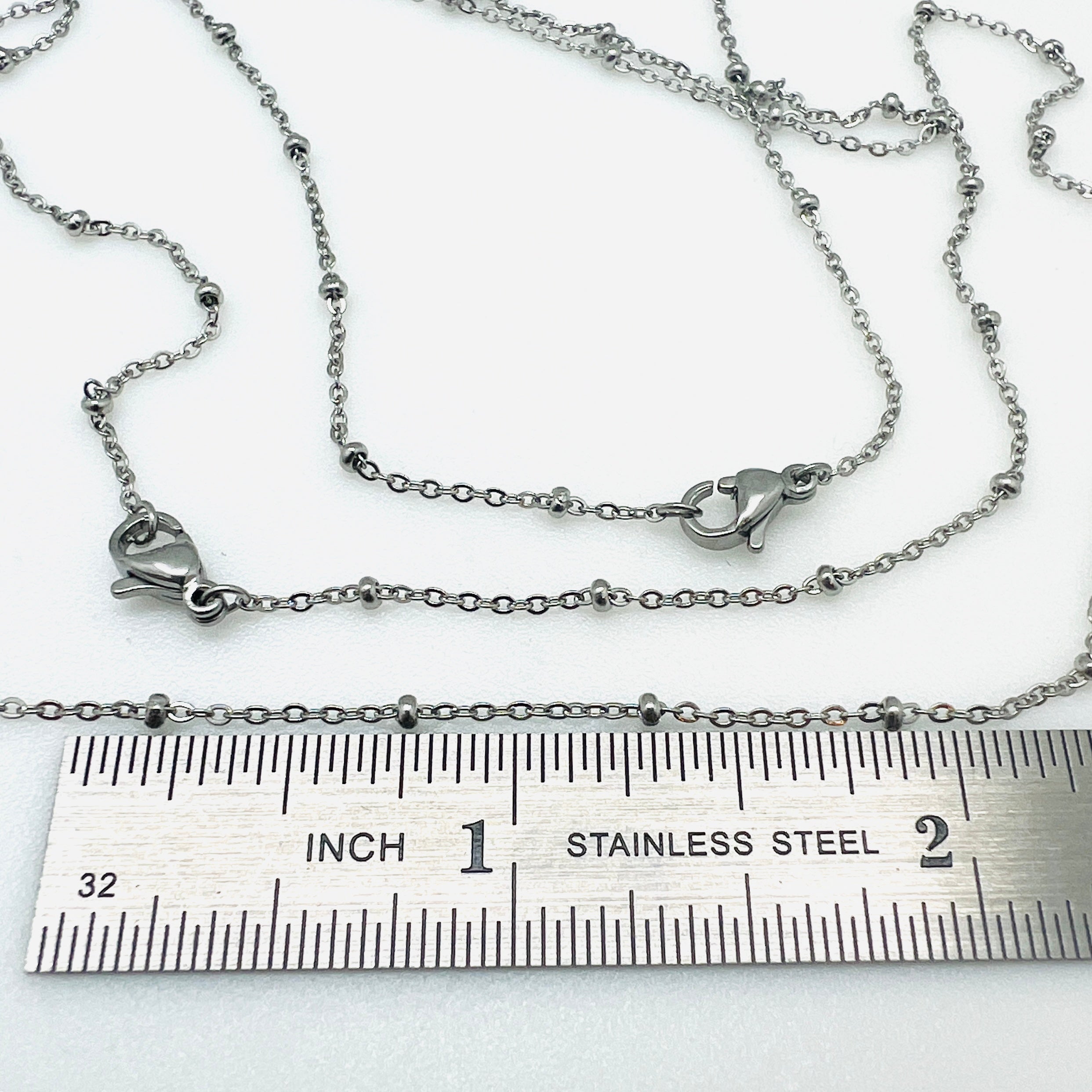 silver tone satellite chain necklace with rondelle beads and lobster claw clasp displayed above ruler with white background.