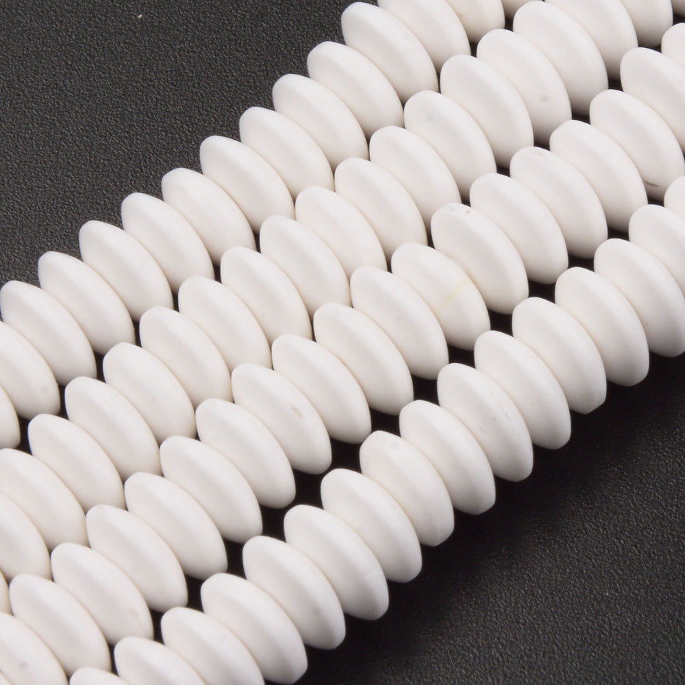 four white polymer clay saucer bead strands over textured black background. 