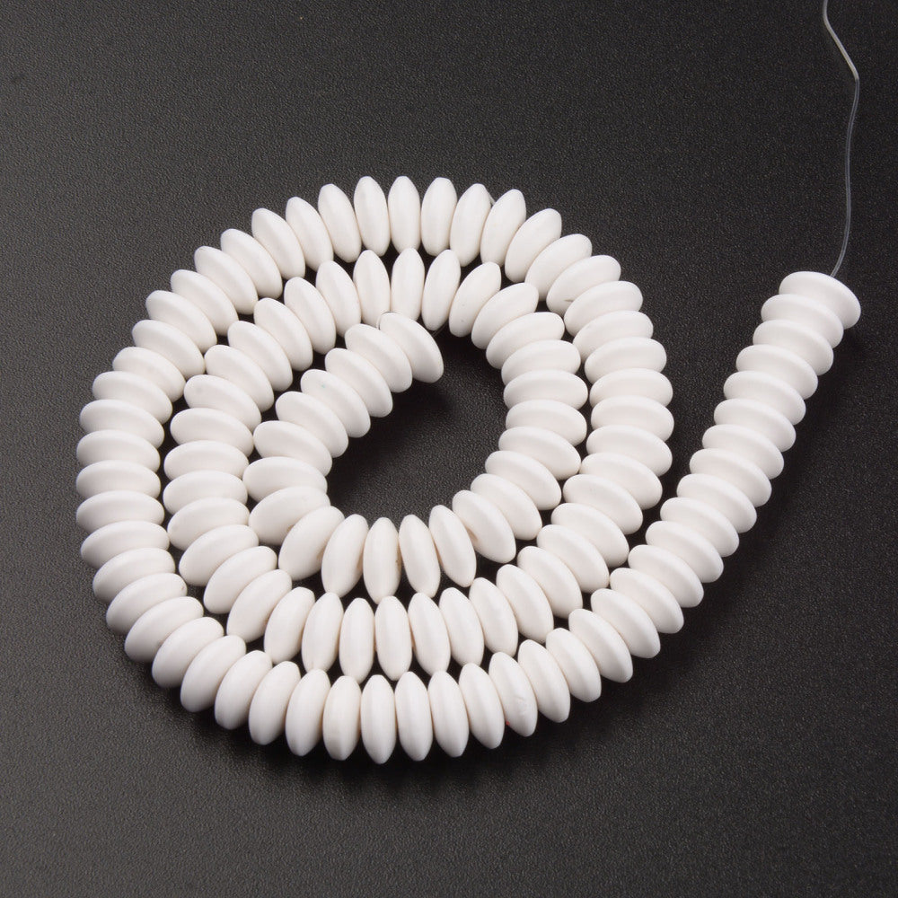 white polymer clay saucer bead strand in a swirl design over textured black background. 