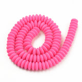 pink polymer clay saucer bead strand in a swirl design over white background. 