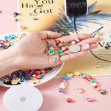light pink surface with a white dish containing most of the bright and adorable beads from the kit while some have spilled onto the surface and some others are strung on elastic cord and a spool of the black cord included in the kit is in the top right corner and a hand displaying some more of the beads and a dollar coin. 