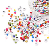 a collection of a large variety of loose beads including seed and white with black letter beads in a crystal bowl and spilled out onto a white surface. 