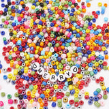 a collection of colorful seed beads with a sample friendship bracelet in the center spelling out "merry" with a heart bead on either side over white surface. . 