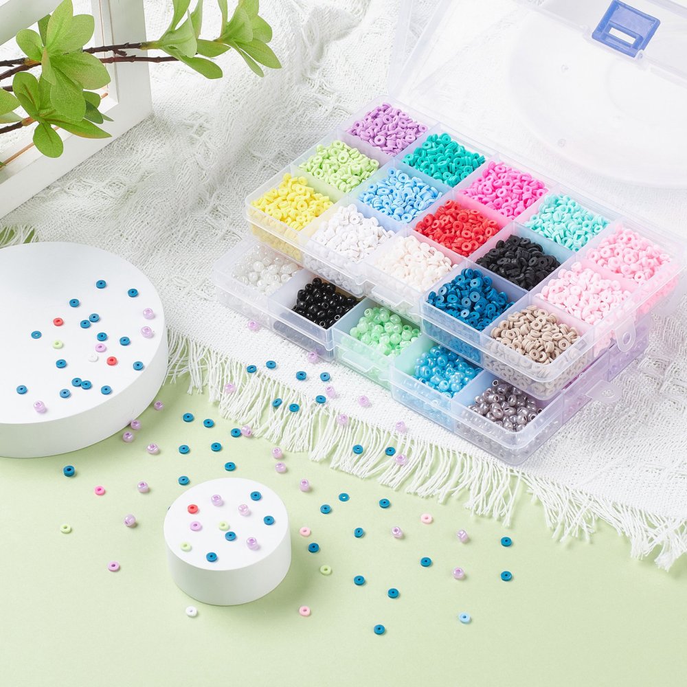twenty of the thirty bead varieties displayed in open plastic containers on a white fringe cloth over light green surface with a peek of a tree branch from the top corner and some of the loose flat disc beads strewn about the photo. 