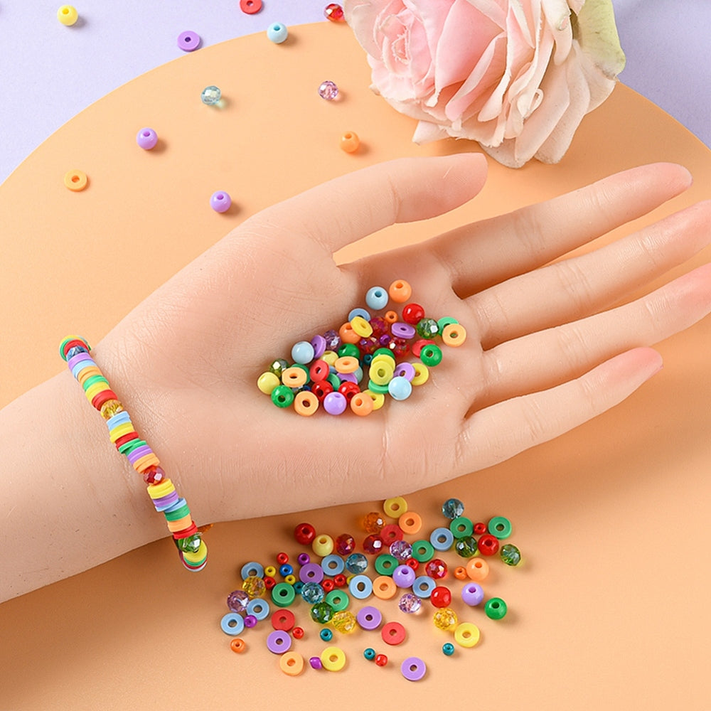 a collection of the wide variety of rainbow beads in a pile on a mannequin hand and on the light purple and orange surface plus a sample bracelet on the mannequin wrist. 