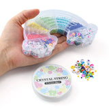 a hand holding the closed bead box with the spool of crystal string and a pile of loose beads on the white surface below. 