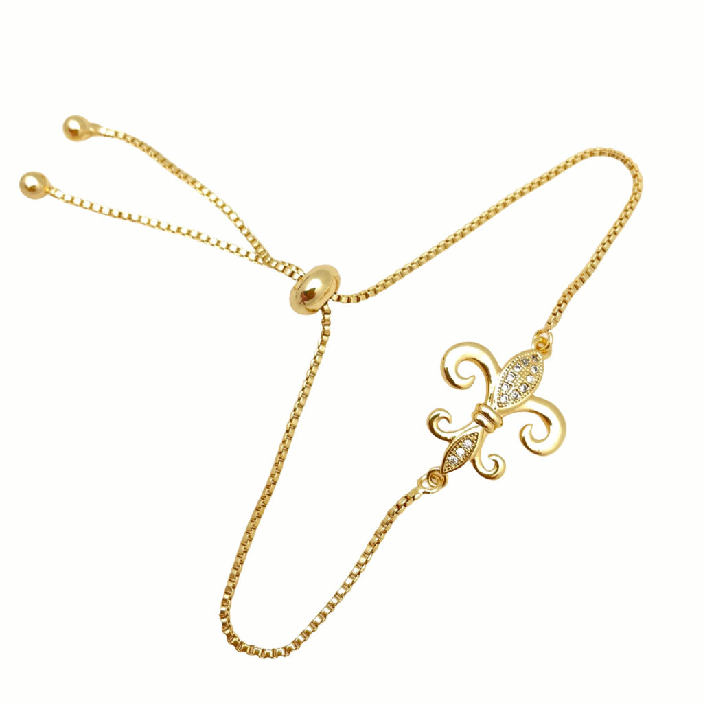 golden, micro pave set clear stone fleur de lis connector and box link bracelet with bolo style adjustable clasp on white background. 