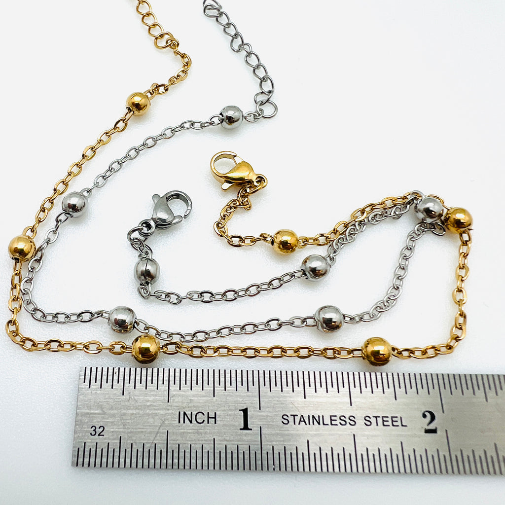 golden and silver tone satellite chain anklets with lobster claw clasp and extender chain displayed above ruler over white background. 