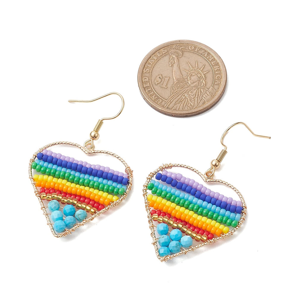 silver tone multicolor dyed magnesite and glass seed bead rainbow heart earrings with ear wires below dollar coin over white background. 
