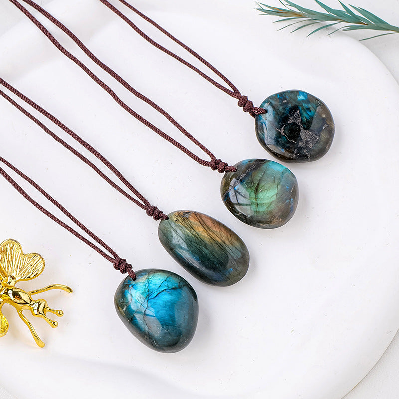 four unique labradorite stone pendants each strung on brown cord over a white background with a golden insect sculpture and rosemary stem .peeking in from the sides. 