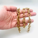 3 golden, large alternating oval and round link chain bracelet with lobster claw clasp displayed on a hand with white background. 
