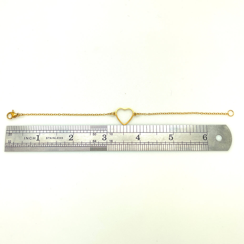 golden cable chain bracelet with center heart focal and lobster claw clasp above stainless steel imperial ruler  on white background. 